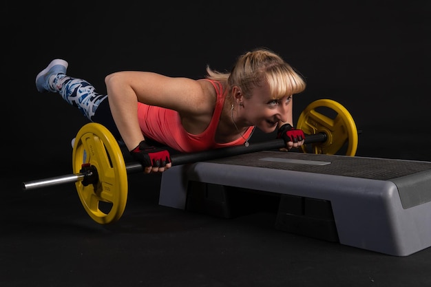 Fitness meisje op een platform met een barbell met dumbbells Sporten op een zwarte