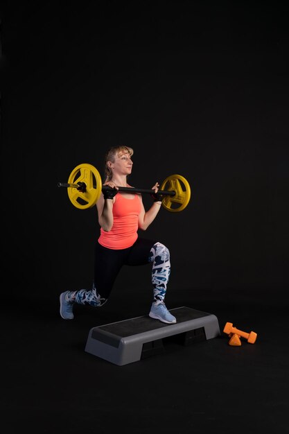 Fitness meisje op een stap platform met een barbell met halters Ga voor sport zwarte achtergrond