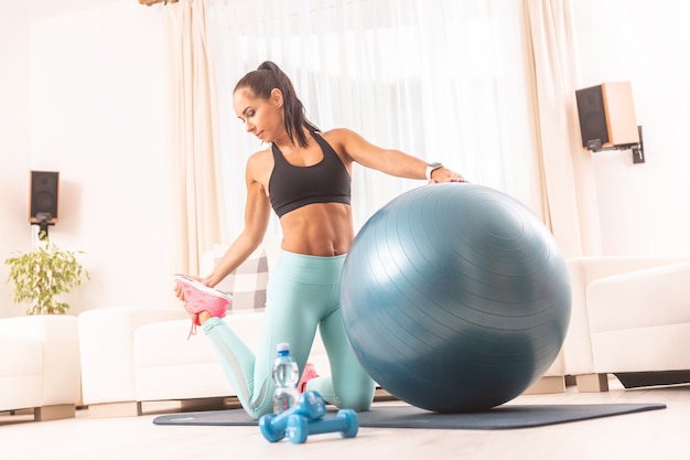 Fitness meisje strekt haar been uit, leunend tegen de blauwe bal voor een thuistraining.