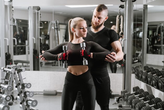 Fitness meisje tillen halter met haar persoonlijke coach in de sportschool