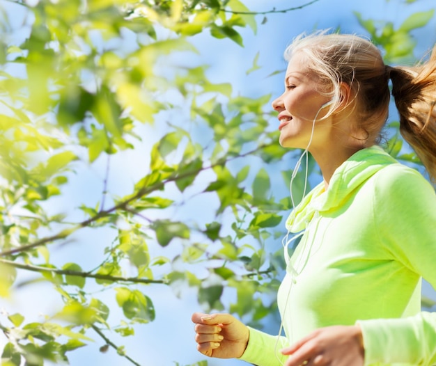 Foto fitness, mensen en een gezond levensstijlconcept - gelukkige jonge vrouwelijke hardloper die buiten jogt