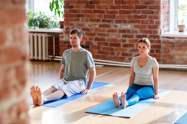 fitness, mensen en een gezond levensstijlconcept - man en vrouw die yoga doen, zittend personeel poseert op matten in de studio