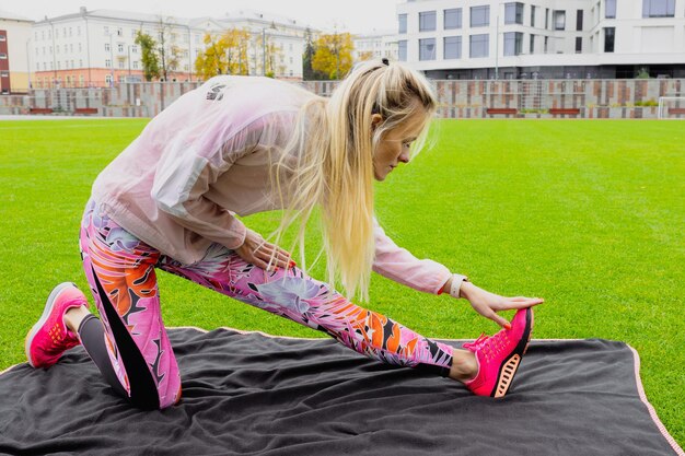 Fitness model in bright sports form shows exercises with dumbbells on a black-pink background