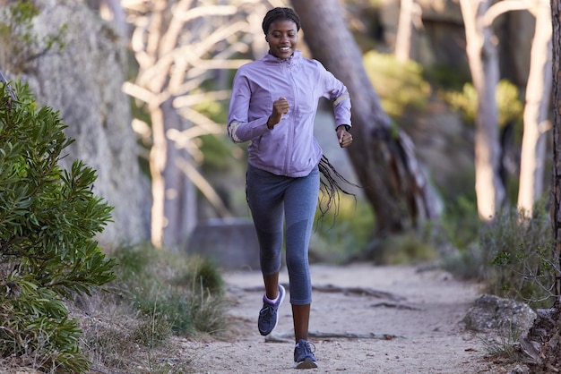 Fitness nature and black woman running for exercise with endurance focus and health in a forest Sports athlete and African lady doing cardio workout or training for race marathon or competition