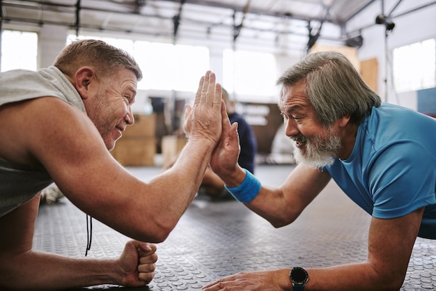 Photo fitness old men on ground and high five for target training goals and excited in gym senior male athletes happy elderly citizens and gesture for achievement exercise or teamwork on ground in gym