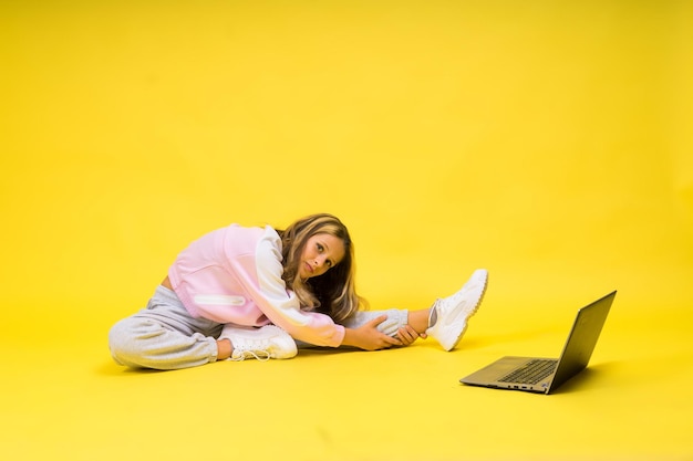 Foto fitness online meisje doet rekoefeningen op de vloer alleen met laptop in de studio