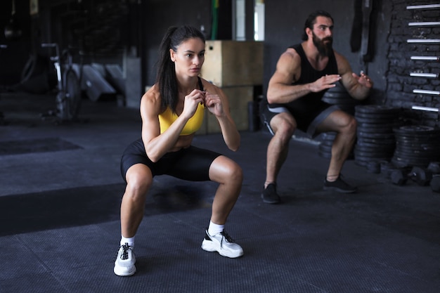 Fitness paar in sportkleding doen squat oefeningen op sportschool.