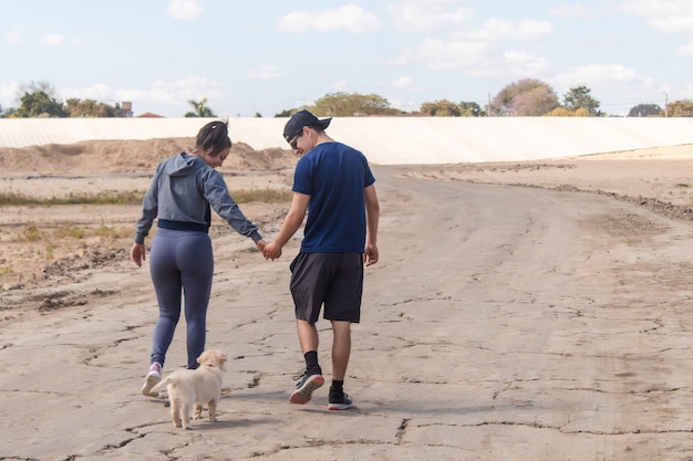 Fitness paar lopen hand in hand met hun puppy op een zandpad.