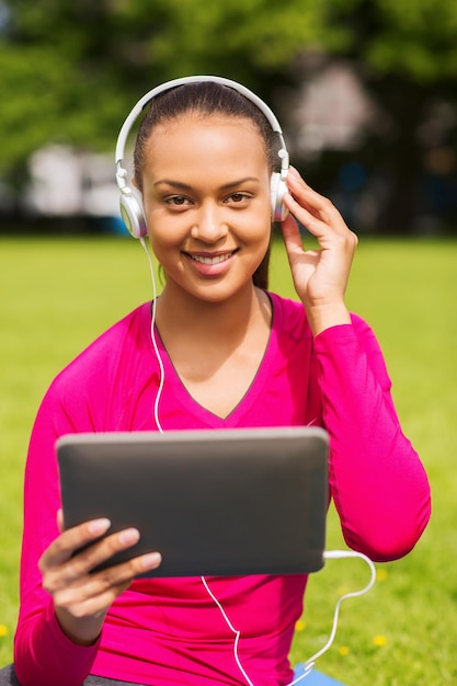 fitness, park, technologie en sport concept - lachende Afro-Amerikaanse vrouw met tablet pc-computer en koptelefoon op mat buitenshuis