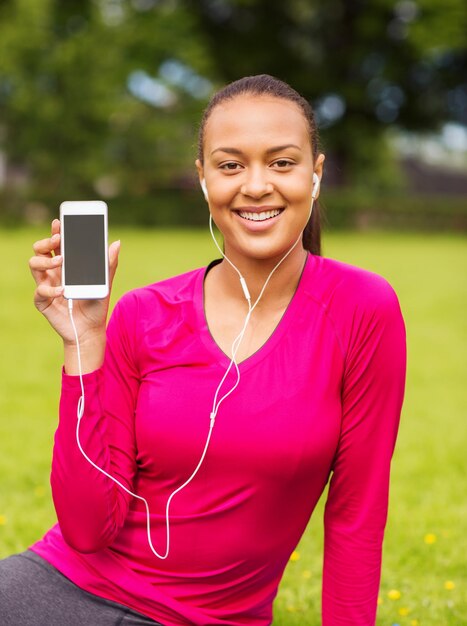 fitness, park, technology and sport concept - smiling african american woman with smartphone and earphones outdoors