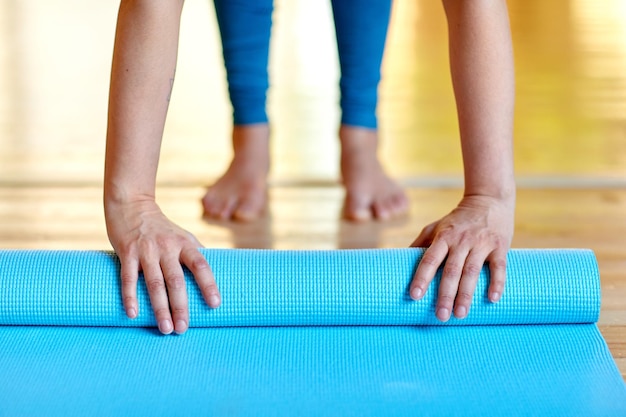 Fitness, people and healthy lifestyle concept - woman hands rolling yoga mat at gym or studio