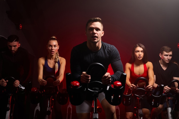 Fitness people in a row exercising with bicycles in a gym. sport, lifestyle and healthcare concept