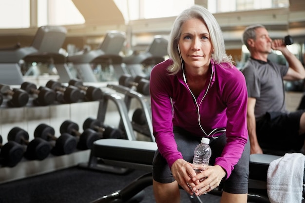 fitness portrait and elderly woman in gym with water bottle for training exercise and workout sports retirement and person with earphones listen to music audio and radio for wellness and health
