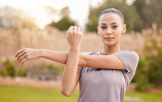 Fitness portrait and woman stretching arms in nature to get ready for workout training or exercise Sports face and young female athlete stretch and warm up to start exercising cardio or running