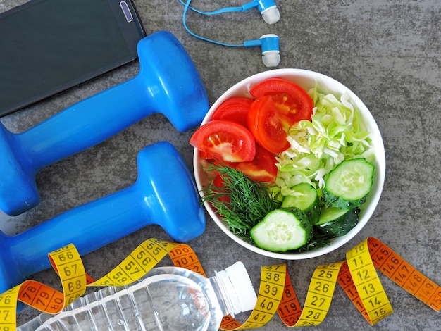 Photo fitness salad, dumbbells and measuring tape