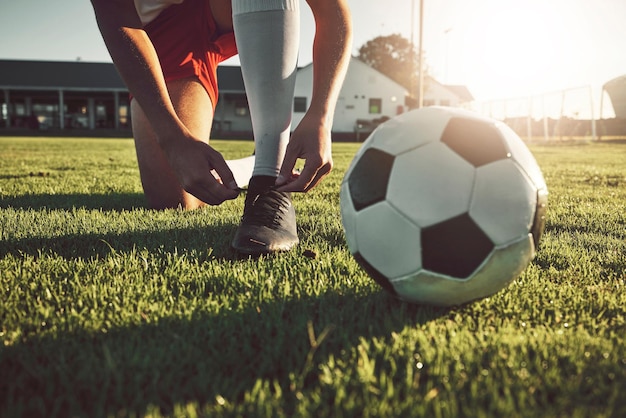 Fitness shoes and soccer player ready for sports training exercise and cardio workout on football field outdoors Hands footwear and athlete tying boots to start a practice game or match