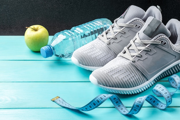 Fitness sneakers, groene appel, meetlint en fles water op blauwe houten achtergrond.