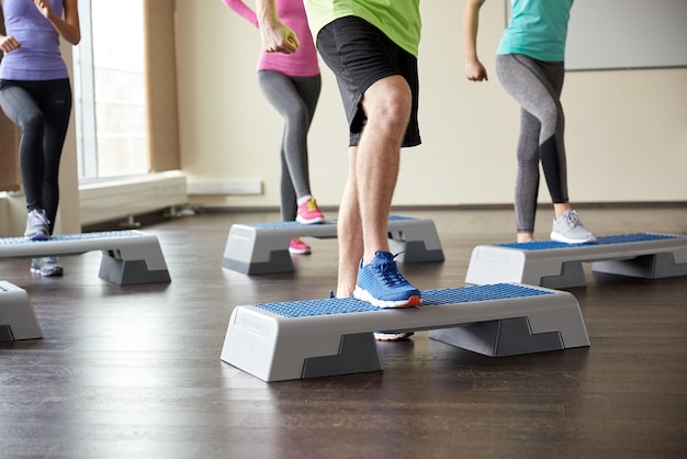 fitness, sport, aerobics en mensenconcept - groep glimlachende mensen die trainen en benen buigen op stapplatforms in de sportschool