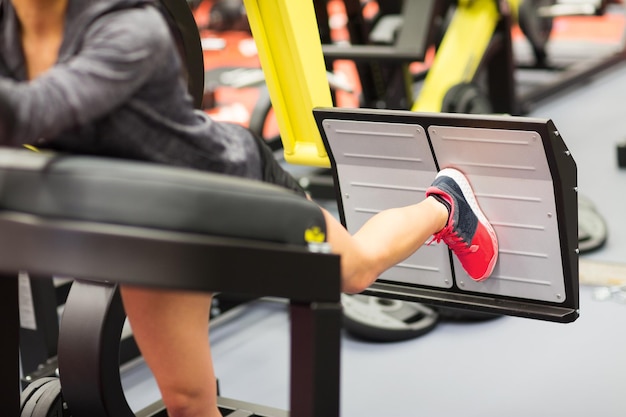 Photo fitness, sport, bodybuilding, exercising and people concept - close up of young woman flexing muscles on leg press machine in gym