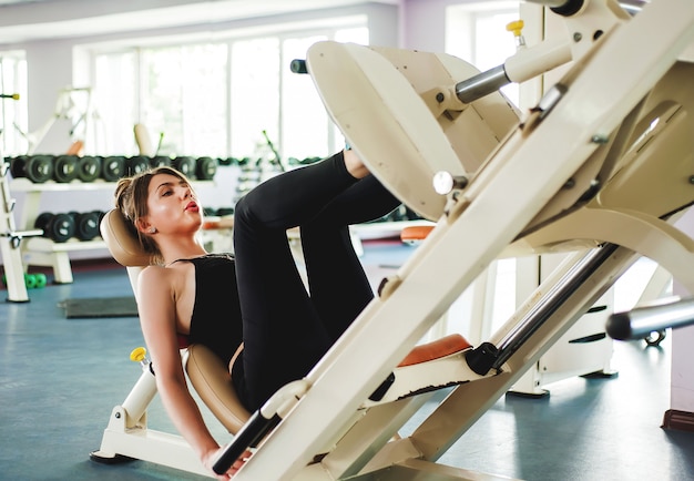 피트 니스, 스포츠, 보디 빌딩, 운동 및 사람들이 개념-체육관에서 다리 프레스 기계에 근육을 flexing 젊은 여자