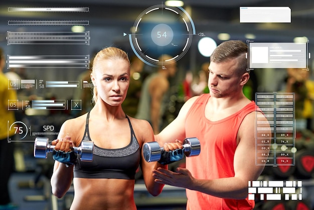 fitness, sport, bodybuilding and weightlifting concept - young woman and personal trainer with dumbbells flexing muscles in gym over virtual charts