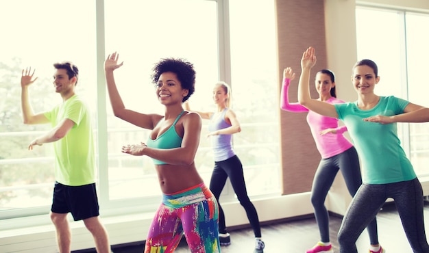 fitness, sport, dance and lifestyle concept - group of smiling people with coach dancing in gym or studio