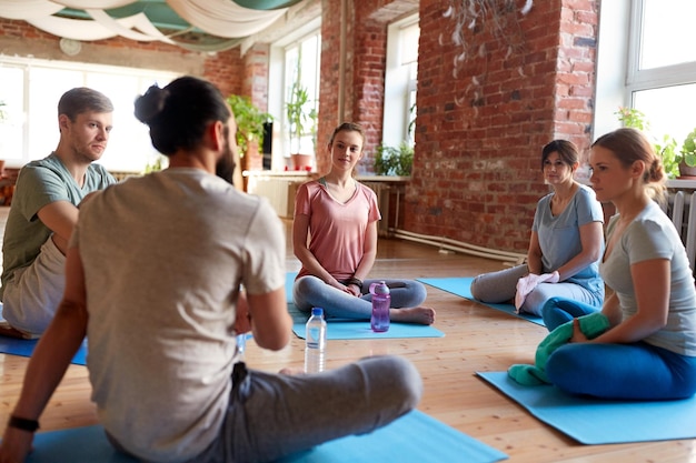 fitness, sport en een gezonde levensstijl concept - groep mensen met waterflessen en handdoeken in yogales rustend op matten in de studio