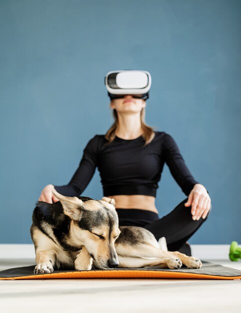 Fitness, sport en technologie. Jonge atletische vrouw VR bril zittend op fitness mat met hond