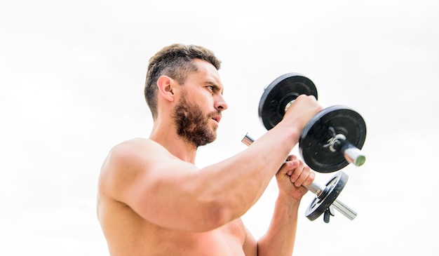 Foto attrezzature per il fitness e lo sport. corpo atletico. palestra con manubri. sportivo uomo con mani forti. steroidi. uomo muscolare che si esercita la mattina con il bilanciere. successo. bicipiti perfetti. tutto è possibile.