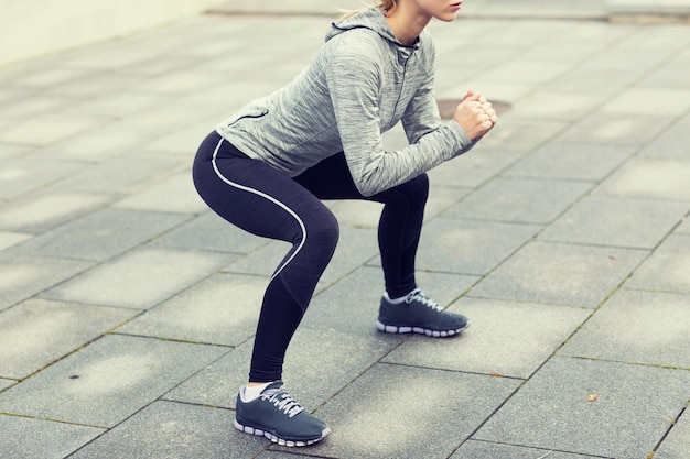 fitness, sport, exercising and healthy lifestyle concept - close up of woman doing squats outdoors