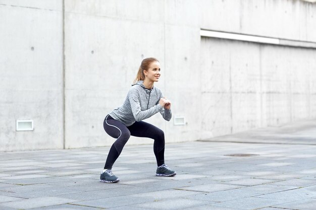 fitness, sport, exercising and healthy lifestyle concept - happy woman doing squats outdoors