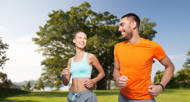 フィットネス、スポーツ、運動、健康的なライフ スタイル コンセプト - 夏の公園の背景にカップルを実行またはジョギングの笑顔