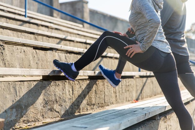 fitness, sport, exercising and lifestyle concept - close up of couple stretching leg on stands of stadium