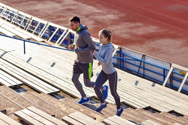 fitness, sport, exercising and lifestyle concept - couple running upstairs on stadium