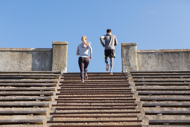 fitness, sport, exercising and lifestyle concept - couple running upstairs on stadium