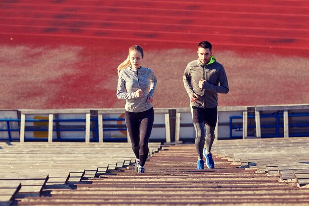 fitness, sport, exercising and lifestyle concept - couple running upstairs on stadium