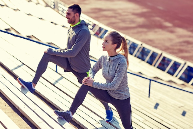 fitness, sport, exercising and lifestyle concept - couple stretching leg on stands of stadium