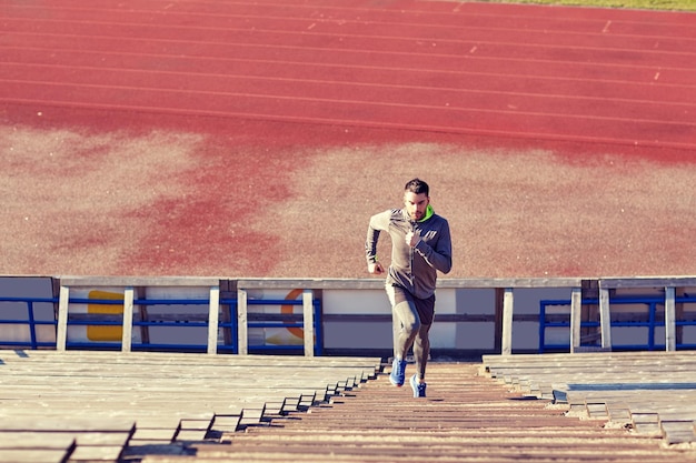 Foto concetto di fitness, sport, esercizio fisico e stile di vita - uomo che corre al piano di sopra sullo stadio