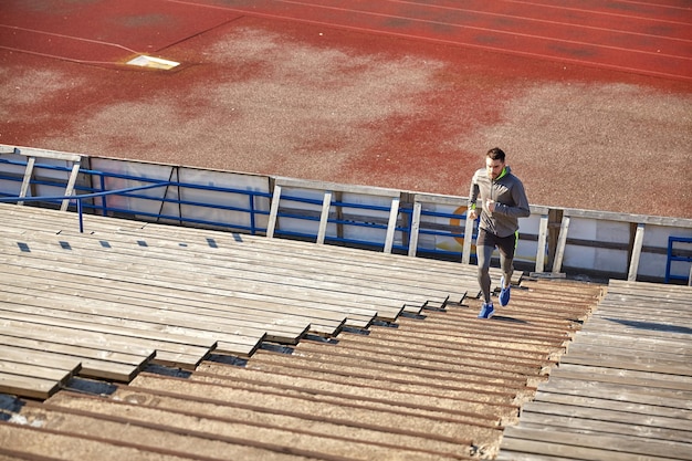 Foto concetto di fitness, sport, esercizio fisico e persone - giovane felice che corre al piano di sopra sullo stadio