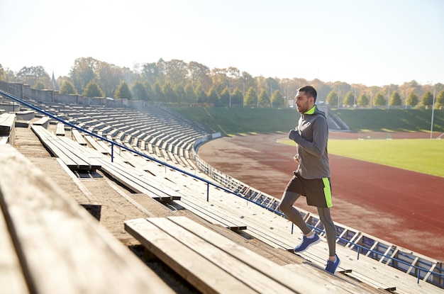 Foto concetto di fitness, sport, esercizio fisico e persone - giovane felice che corre al piano di sopra sullo stadio