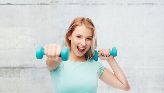 fitness, sport, exercising and people concept - smiling beautiful sporty woman with dumbbell in fight stand over gray concrete wall background