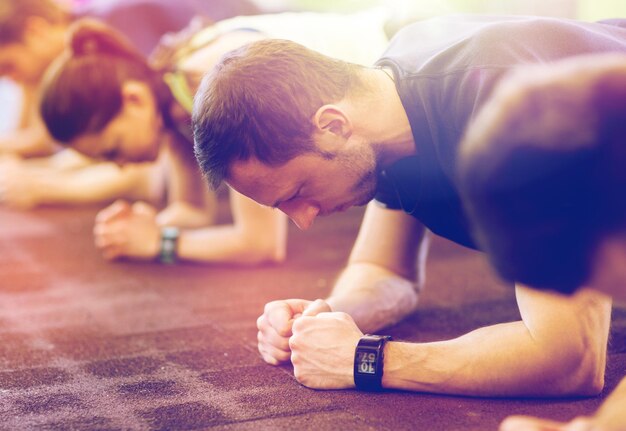 Foto fitness sport esercizio fisico persone e stile di vita sano concetto uomo con tracciatore cardiaco all'allenamento di gruppo facendo esercizio di tavola in palestra