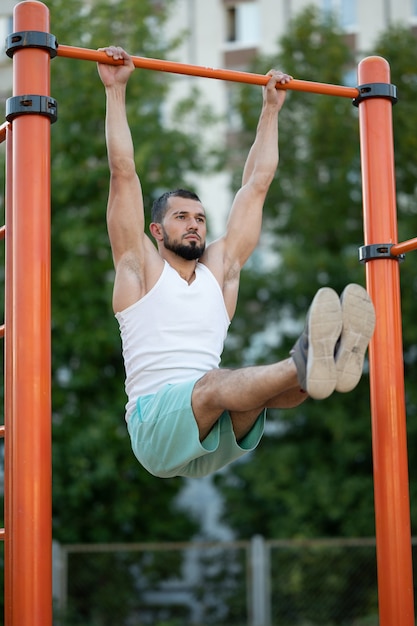 사진 피트니스, 스포츠, 운동, 교육 및 생활 양식 개념-여름 공원에서 가로 막대에 복부 운동을하는 젊은 남자