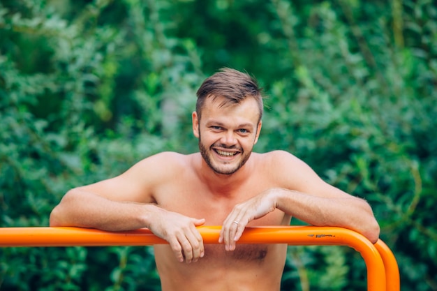 Fitness, sport, exercising, training and lifestyle concept - young man doing triceps dip on parallel bars outdoors. smile