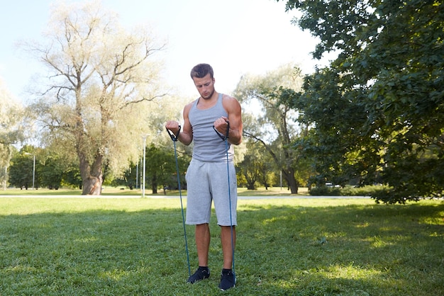 Fitness, sport, exercising, training and lifestyle concept - young man exercising with expander in summer park