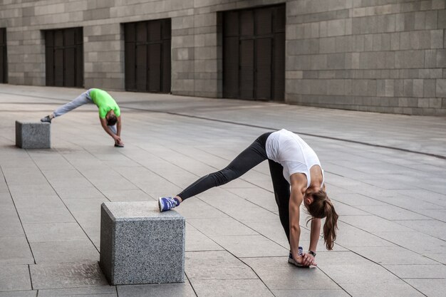 Fitness, sport, exercising, training and people concept - couple doing triceps dip exercise on city street bench.