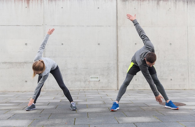 fitness, sport, exercising, training and people concept - couple stretching on city street