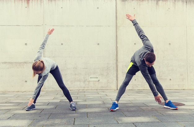 fitness, sport, exercising, training and people concept - couple stretching on city street