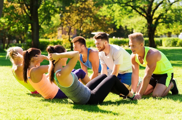 fitness, sport, friendship and healthy lifestyle concept - group of happy teenage friends or sportsmen exercising and doing sit-ups at boot camp