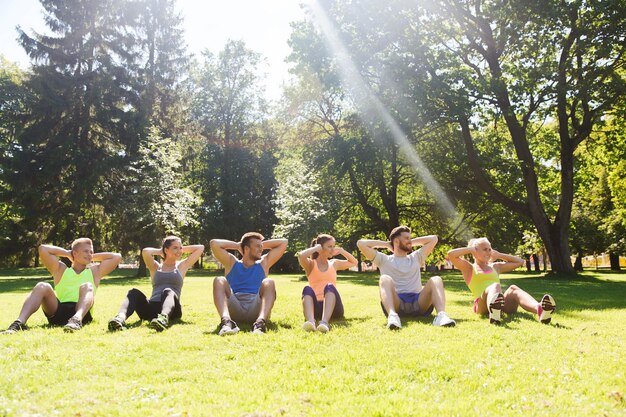 fitness, sport, friendship and healthy lifestyle concept - group of happy teenage friends or sportsmen exercising and doing sit-ups at boot camp